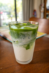 Ice milk matcha green tea in clear glass, home made Japanese style, on brown wooden table in house