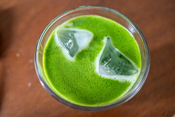 Ice milk matcha green tea in clear glass, home made Japanese style, on brown wooden table in house