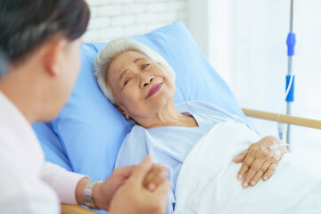 Fototapeta premium Asian man visiting his elderly mother in hospital and they have a conversation together.