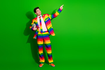 Young man in a rainbow patterned suit holding a disco ball, pointing cheerfully against a vibrant...