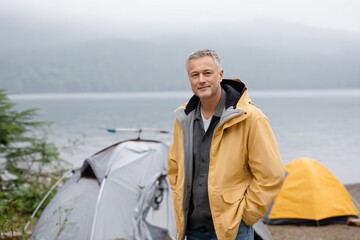 Fototapeta premium A man in a yellow jacket stands in front of a tent. He smiles and looks at the camera. The concept of travel and adventure