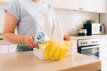 Female adult organizing cleaning supplies in modern kitchen interior