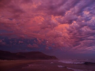 A tranquil beach scene at sunset with vibrant clouds reflecting warm hues, serene waters, and a peaceful atmosphere in Nature's valley, South Africa