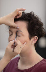 Obraz premium Professional beautician applying makeup on beautiful young woman's face. Professional make up studio work with gorgeous female model.