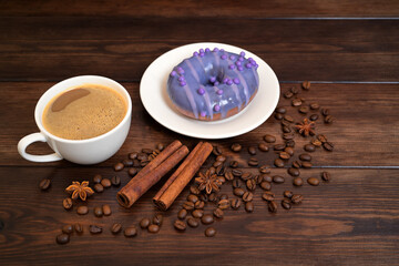 Cup of Coffee and Purple Donut with Cinnamon and Coffee Beans on Wooden Table