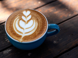 A cup of cappuccino coffee, with a blue cup placed on a black wooden table. Beautiful latte art...