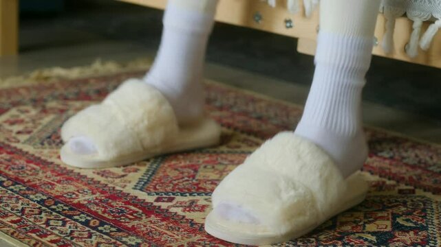 Woman dances with feet in white slippers while sitting on bed. Fun dance day captured in close-up on floor carpet. Joyful dance movements show happy day fun. Happy fun woman in home 