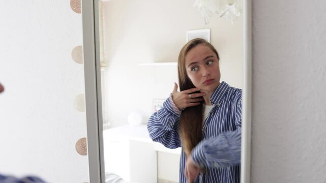 Teenage girl doing her hair in front of the mirror. Daily routine.