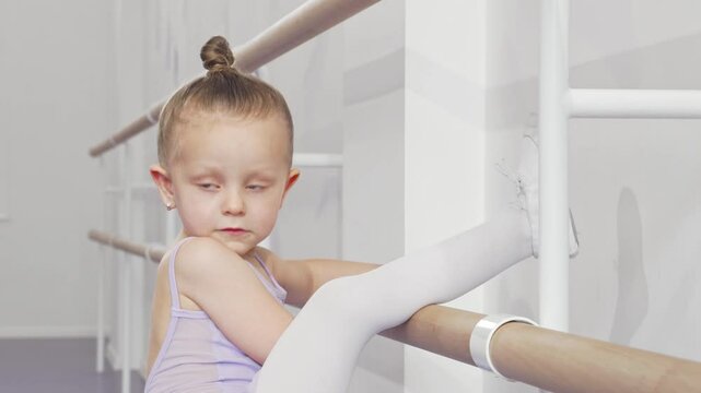 Charming little ballerina girl stretching her leg on ballet barre