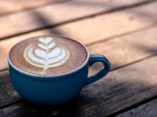 A cup of cappuccino coffee, with a blue cup placed on a black wooden table. Beautiful latte art...
