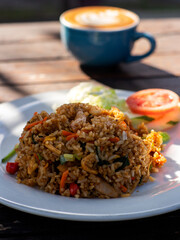 Fried rice on a white plate, with a cup of coffee in the background. Traditional Indonesian cuisine. Asian food.