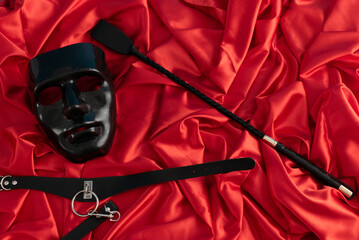 Adult sex games. Kinky lifestyle. Mask and whip ridding crop on the red linen. Bdsm outfit