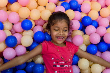 Obraz premium Girl joyfully plays in ball pit at indoor playground
