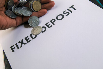 Hand holding coins over a fixed deposit document