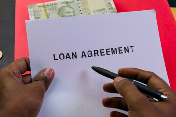 Hands signing loan agreement with cash on table