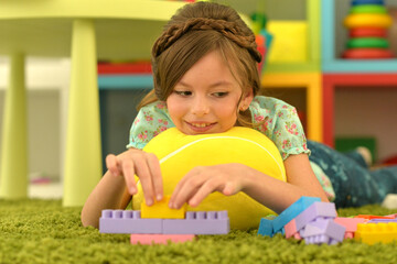 Portrait of cute girl playing with colorful plastic blocks in room