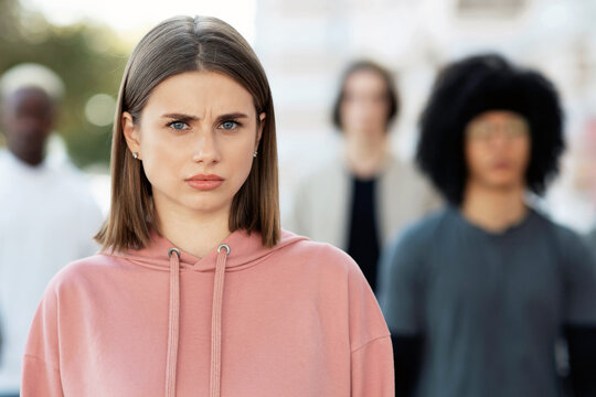 Indignant young lady standing over multiracial group of students, looking at camera, closeup. Millennial men and women striking on the street, fighting against racism and descrimination