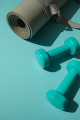 Sport or workout concept flat lay with blue dumbbells and yoga mat on the blue teal background. Copy space