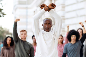 Black guy activist leading international group of young people, raising locked hands up and looking...