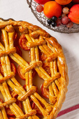 Apricot pie decorated with dough ornament and a metal basket with fruits and berries.