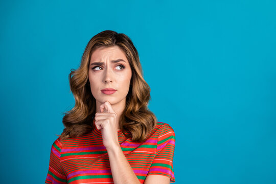Young woman in a colorful striped shirt deep in thought against a blue background