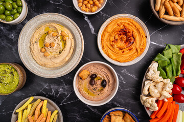 Various hummus dips. Hummus plate with vegetable snacks. Carrot, cucumber, tomato, celery sticks, dry crackers and olive, top view. Vegan and traditional hummus as healthy and vegan snack.