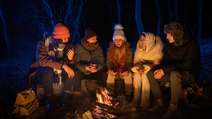 Friends sitting around a campfire in the woods on a winter evening