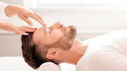 Unrecognizable masseuse hands rubbing sleeping middle-aged man forehead, making relaxing head...