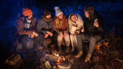 Friends sitting around a campfire in the woods on a winter evening