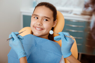 Dental office and pediatric dentistry. African american doctor in rubber gloves with stomatology tool for treats tooth of smiling little child in medical chair in clinic, pov, close up, copy space
