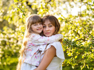 Happy mother and daughter together outdoors. Hugging and playing in spring blooming garden. Mother's Day