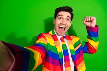 Cheerful man in a vibrant rainbow-striped suit expressing excitement against a bright green...