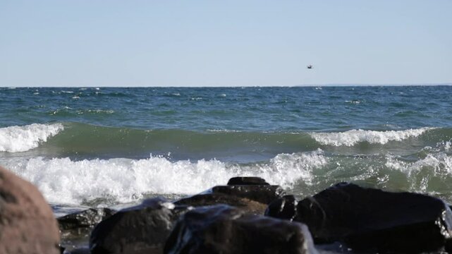Big slow motion waves rolling into rocky shore in early evening with seagull flying through the sky, Lake Superior, Duluth, Minnesota, United States