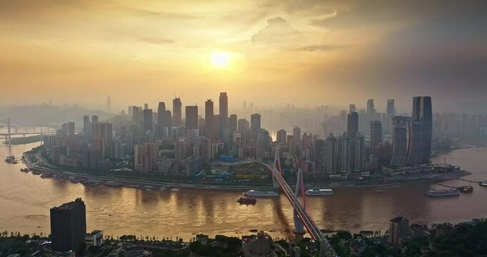 Aerial shot of Chongqing cityscape skyline silhouette with bridge over the river during a hazy golden sunset in China.