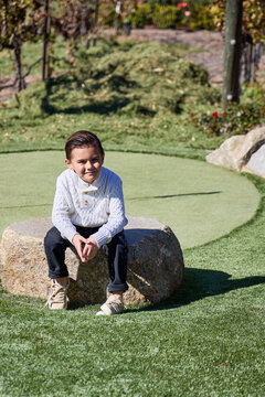 A young boy sits on a rick near a putting green