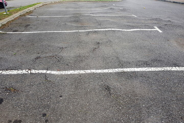 An empty parking lot features multiple cracked asphalt surfaces by trees roots