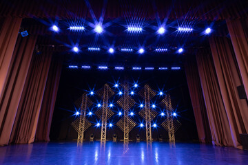Stage illuminated by vivid red and amber lights, featuring a symmetrical truss structure with diagonal light panels and reflective flooring, creating a dramatic ambiance.