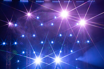 An array of stage lights emits vivid purple and blue beams, forming radiant starburst effects and a...