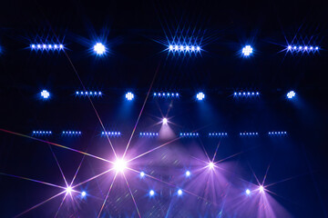 Stage illuminated with vivid blue and white lights, producing lens flares and decorative spot...