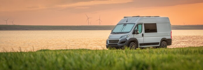 panoramic view to white isolated camper van on green meadow infant of sea shore in sunset time with copy space