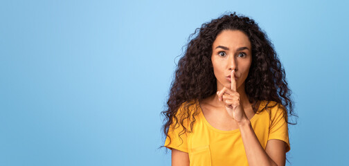 Keep silence. Serious young woman showing shhh sign at camera, holding finger near lips, mysterious...