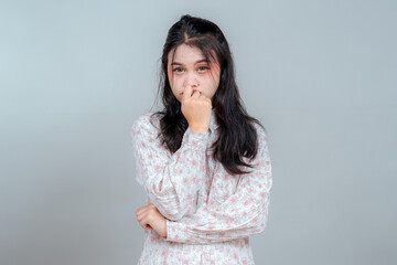Close-up portrait of an anxious young Asian woman biting her thumb while looking worried and...