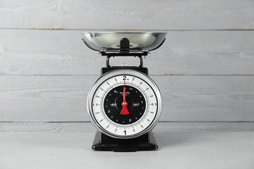 Mechanical kitchen scale with bowl on grey textured table against wooden background