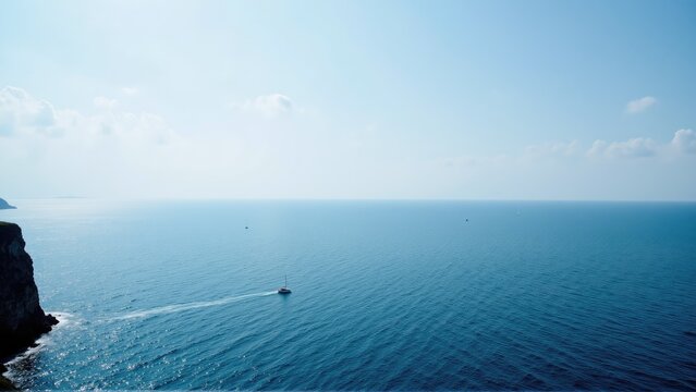 coastal cliff ocean photogenic. A serene seascape featuring a calm ocean and distant sailboats under a clear blue sky, perfect for relaxation or travel themes.
