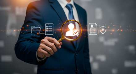 Businessman in Dark Blue Suit Holding Magnifying Glass Over Digital Icons Against Gray Background