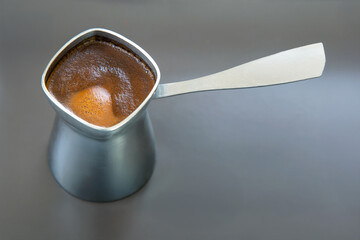 Stylish close-up of a cezve with aromatic Turkish coffee on a gray surface. Ideal for modern cafe decor, coffee recipes, or minimalist food styling projects.