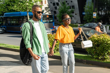 Laughing happy African American couple walking hand in hand through city streets, enjoying date. Joyful man and woman companionship, romantic love and city exploration, shared carefree walk together