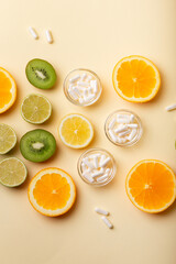 White vitamin C capsules and fruits such as kiwi, lime, lemon and orange as a natural source of vitamin C on beige background, top view. Natural vitamins and vitamin pills. Healthy lifestyle.