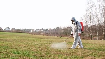 Man wearing protective suit treats the lawn from insect parasites using poison sprayer. Weedkiller. Gardener in a full face mask respirator with personal protective equipment. High quality 4k footage.
