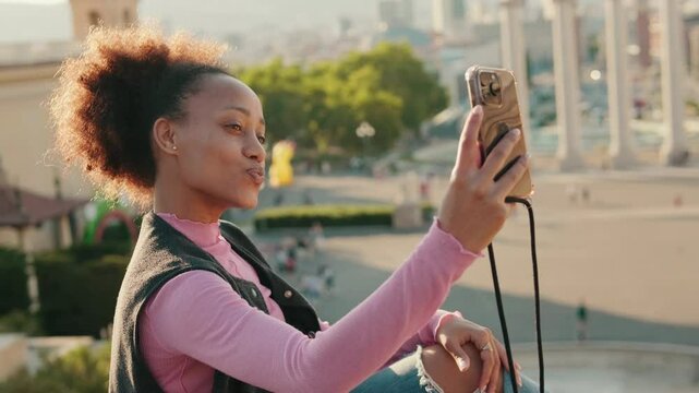 Happy young woman takes a selfie in Barcelona, Spain overlooking the National Art Museum of Catalonia. She smiles and makes a kissy face.